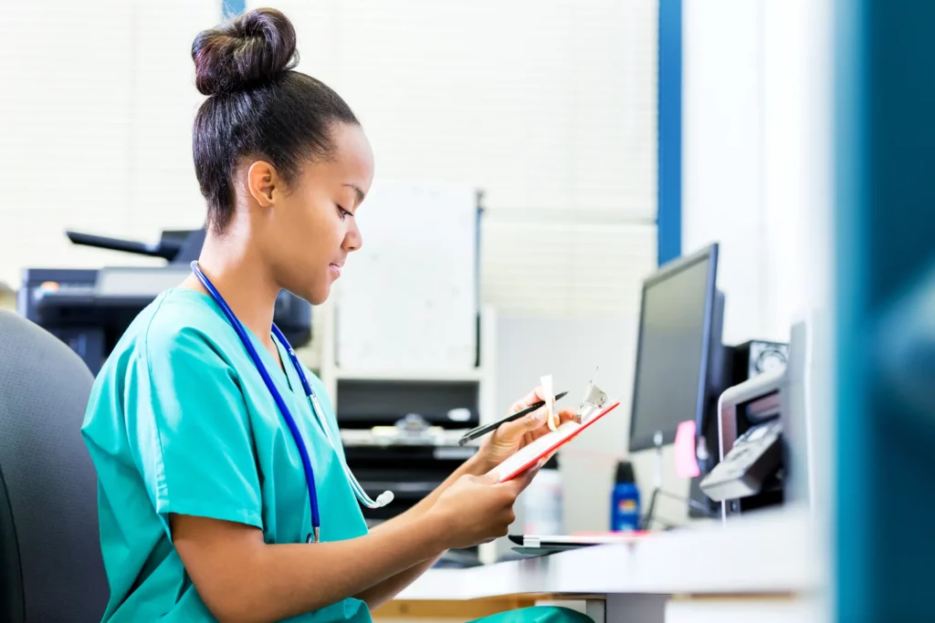 Medical Biller cute african american girl behind desk working and wearing scrubs
